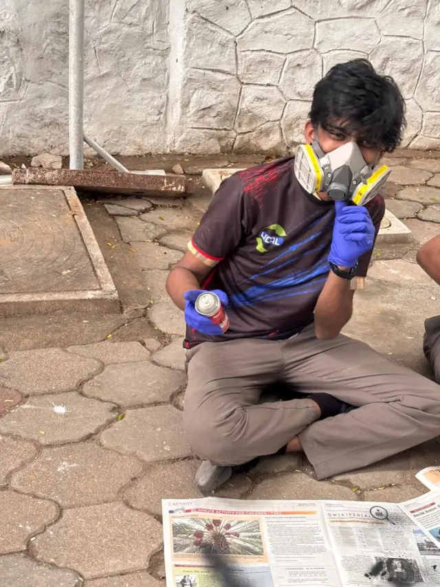 Adithya in a respirator and gloves, spray-painting the car on the ground