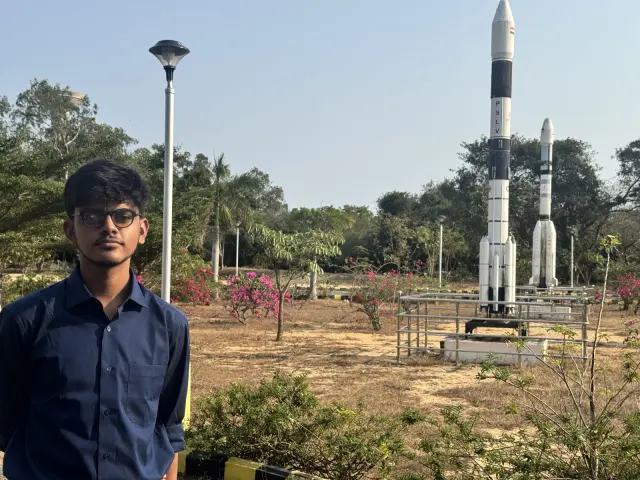 Adithya beside a full-size launch vehicle model under a blue sky