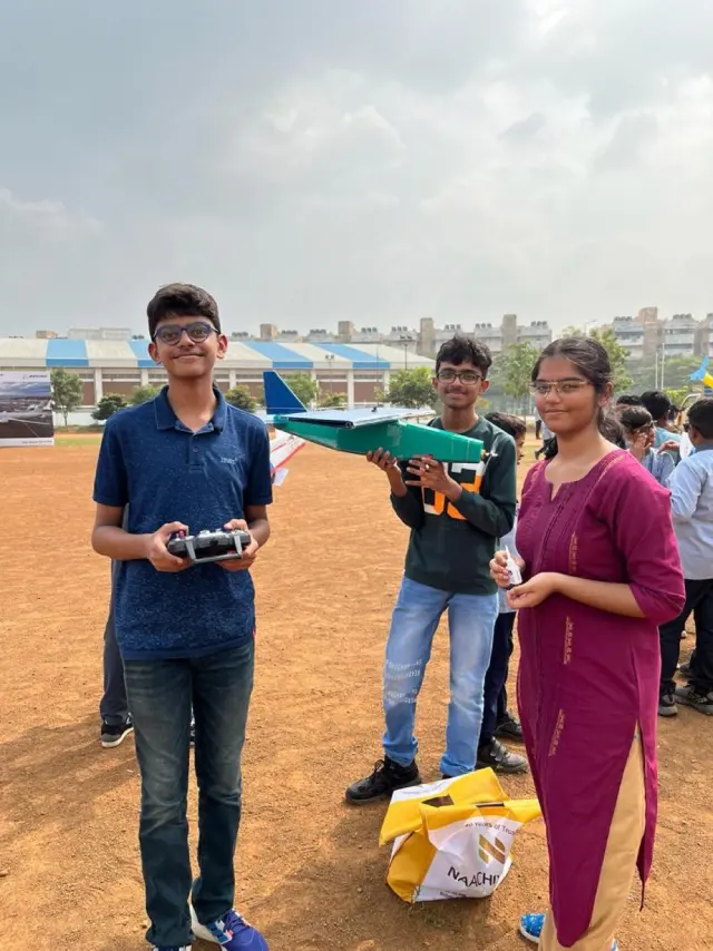 Adithya holding the radio transmitter on the IIT Madras field, with two teammates and the green-and-white cargo plane